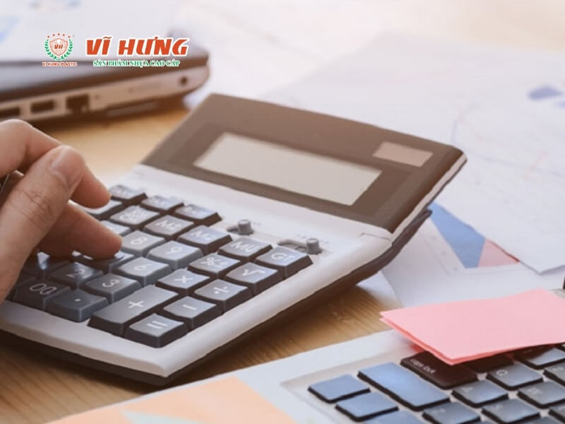 Tay người đang sử dụng máy tính, chuột máy tính, và các giấy tờ tài chính trên bàn làm việc, biểu thị quá trình lập kế hoạch tài chính và tính toán chi phí kinh doanh