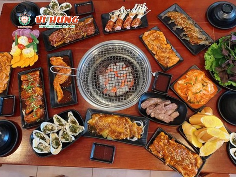 Nhìn từ trên xuống bàn lẩu nướng được setup đầy đủ với bếp nướng trung tâm, các khay nguyên liệu thịt hải sản và rau củ bày xung quanh gọn gàng.