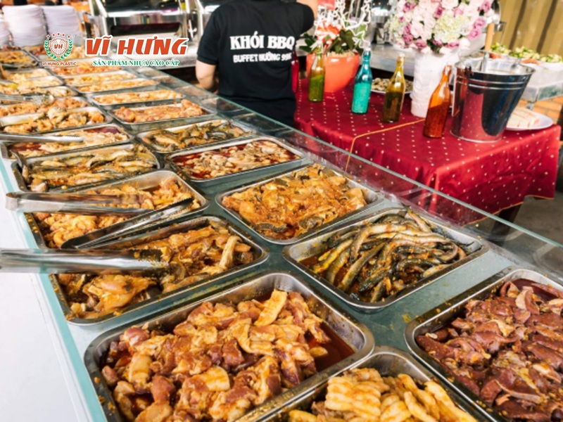 Quầy buffet lẩu nướng với hàng chục khay thức ăn đa dạng gồm thịt, rau củ và hải sản được bày sẵn phục vụ khách tự chọn.