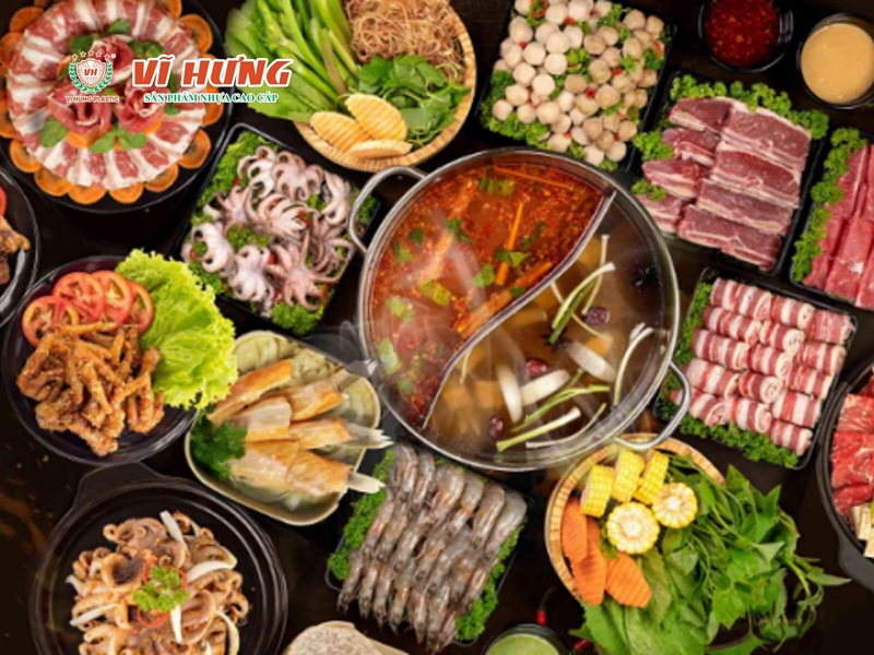 Nhìn từ trên xuống bàn lẩu nướng đầy đủ với nồi lẩu Thái đỏ, các đĩa thịt bò, hải sản, rau củ và nấm bày xung quanh