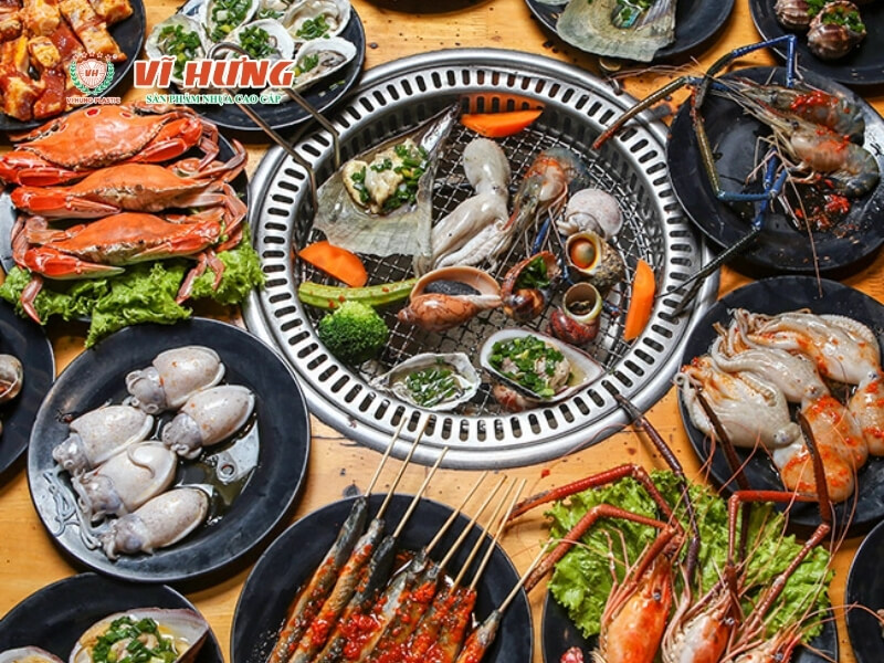 Mâm hải sản nướng buffet gồm cua, tôm, hàu, mực và nhiều loại hải sản tươi sống bày trên bếp than và các đĩa xung quanh