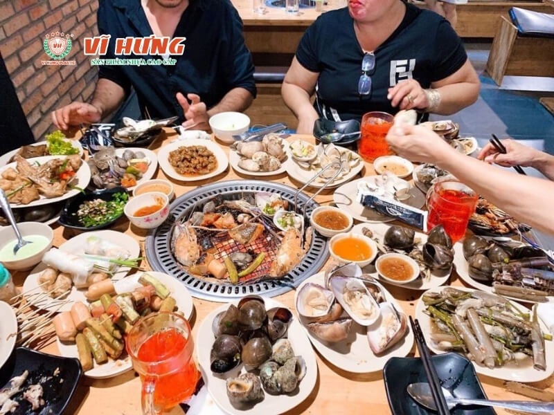 Nhóm khách đang ăn buffet nướng tại nhà hàng, bàn đầy món hải sản, đồ nhậu và nước uống đi kèm