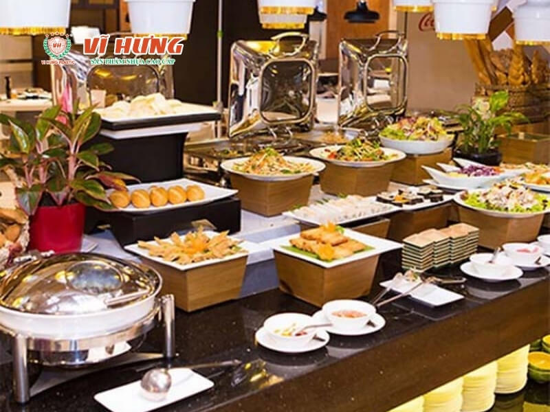 Quầy buffet trong nhà hàng với nhiều món ăn trình bày gọn gàng dưới đèn giữ nhiệt, gồm salad, món chiên và bánh, sẵn sàng cho khách tự phục vụ
