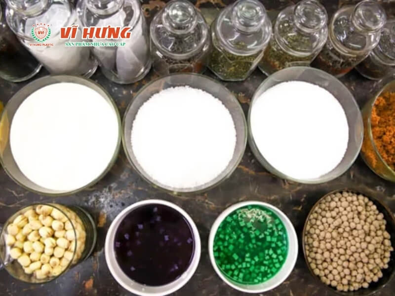 Các hộp chứa nguyên liệu trà sữa được sắp xếp gọn gàng gồm ba bát sữa trắng lớn, các hộp nhỏ chứa trân châu đen, thạch xanh lá, đậu trắng, siro cam, và các loại gia vị khác