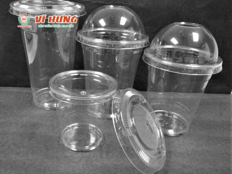 Các loại cốc nhựa trong suốt theo kích cỡ khác nhau, nắp cốc đóm cong, nắp cốc phẳng, và các phụ kiện bao bì khác được sắp xếp trên nền xám