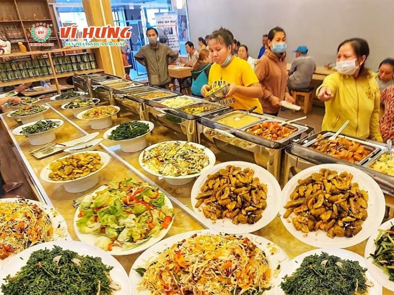 Quầy buffet chay với hàng chục món được bày trên đĩa lớn và khay inox, thực khách đang chọn thức ăn trong không gian nhà hàng đông đúc.