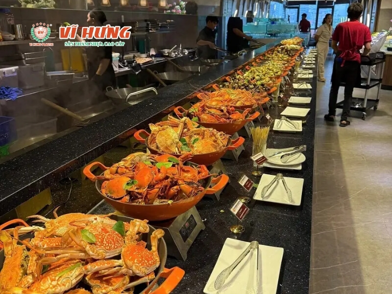Quầy buffet hải sản cao cấp với hàng chục nồi cua hấp màu cam xếp dài trên mặt bàn đá đen, nhân viên bếp đang làm việc phía sau trong không gian nhà hàng hiện đại.