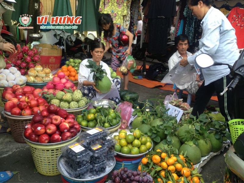 Sạp trái cây vỉa hè với xe đẩy, rổ nhựa và trái cây tươi bày ngoài trời